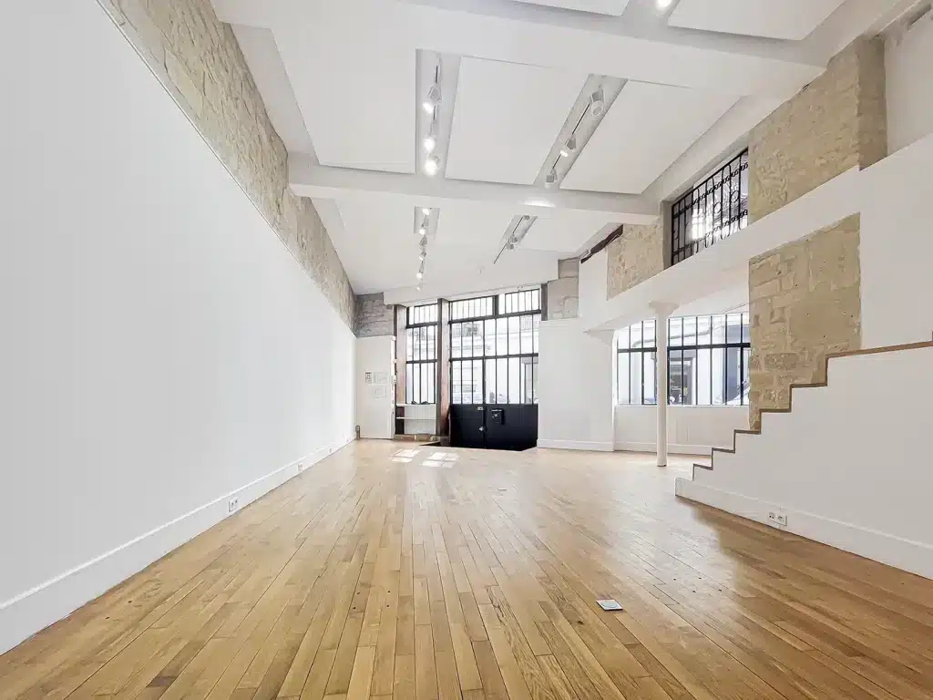 Salle polyvalente à louer au 66 Rue Charlot, avec sol en bois clair et murs blancs, idéale pour des événements.