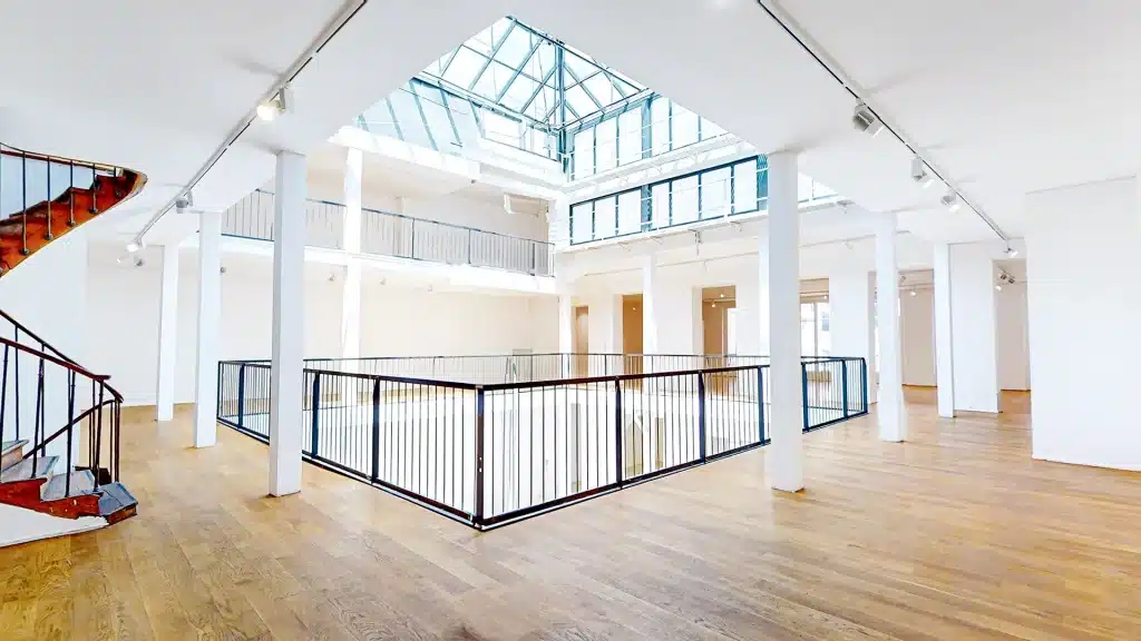 Vaste atelier sous verrière du Marais baigné de lumière zénithale, murs blancs et sol clair, Galerie Joseph