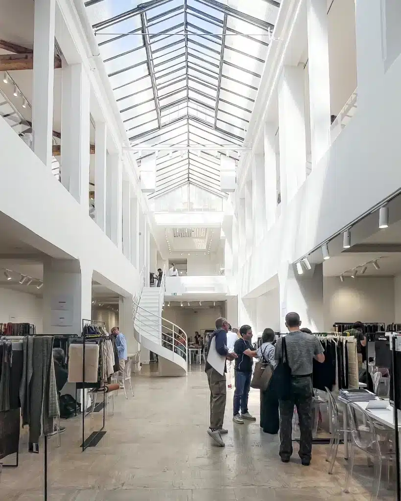 Intérieur d’une galerie aux murs blancs dans le Marais, portants de vêtements soigneusement présentés et invités en petit comité